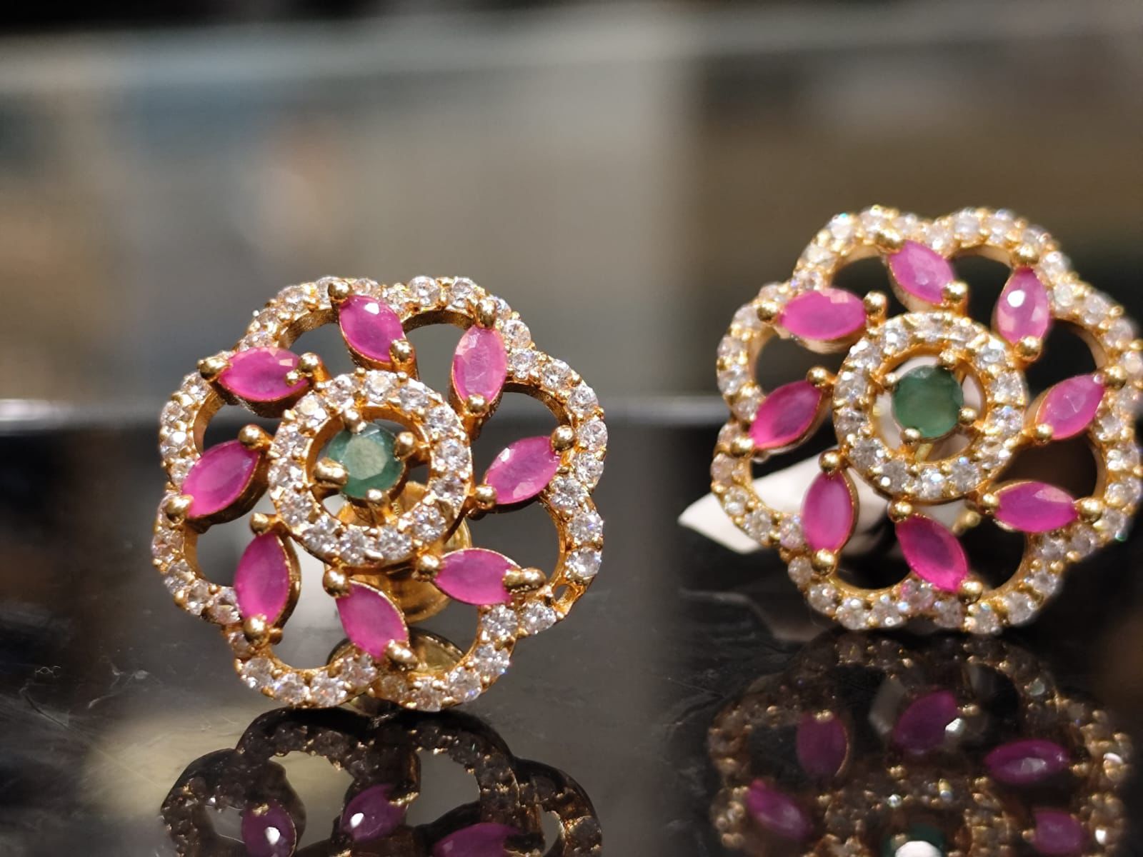 Floral stud earrings with pink and green stones.