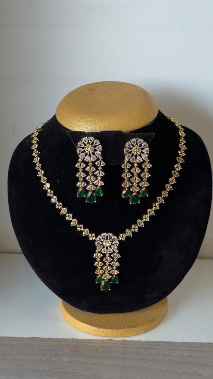 Gold toned necklace with a geometric white stone chain and a tiered floral pendant finished with emerald-green teardrops.