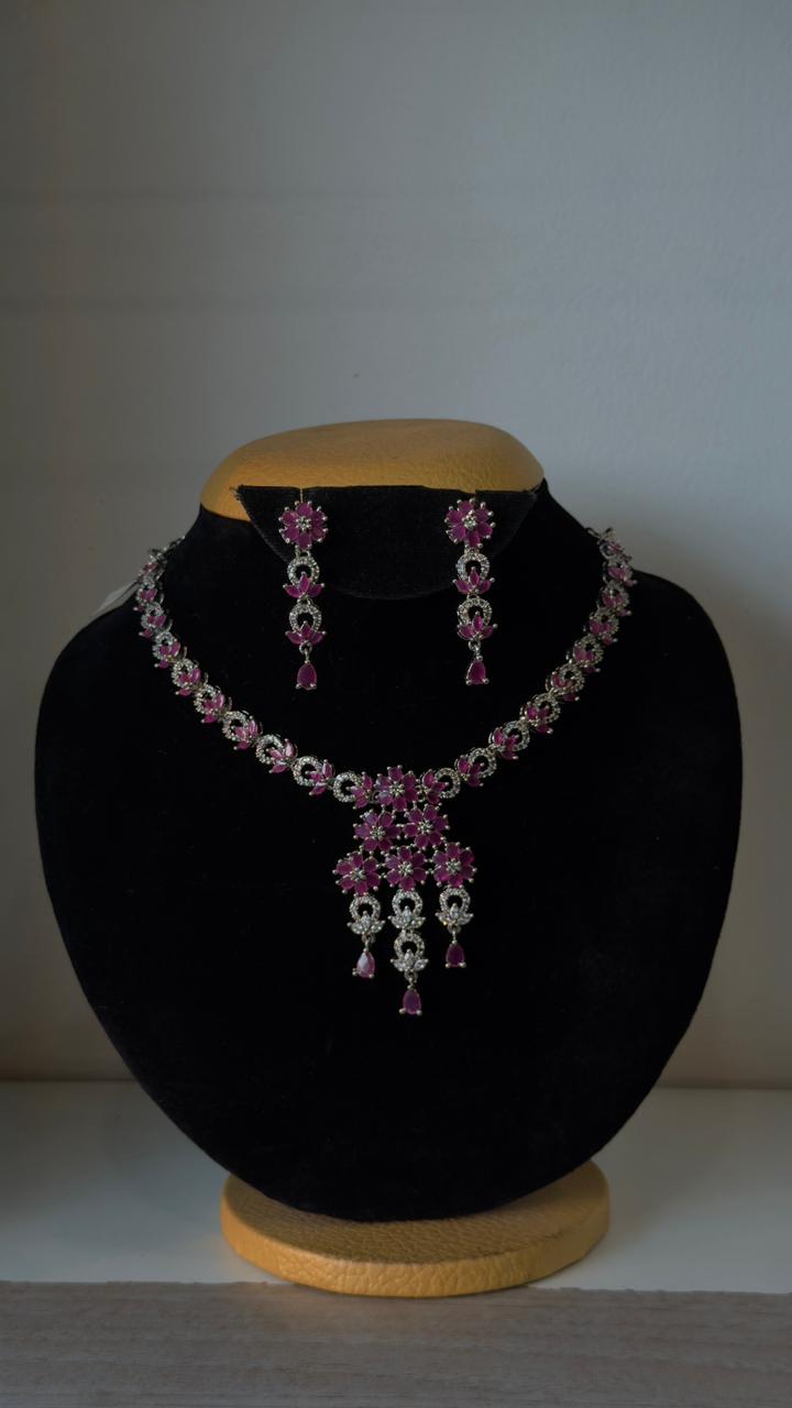 Silver-toned necklace with a cascading floral centerpiece made of vibrant pink stones.