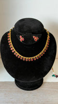 Gold toned necklace lined with a single row of oval-shaped, ruby-red stones.